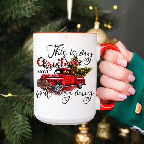 White mug with red truck design and text held by a person in front of a Christmas tree.