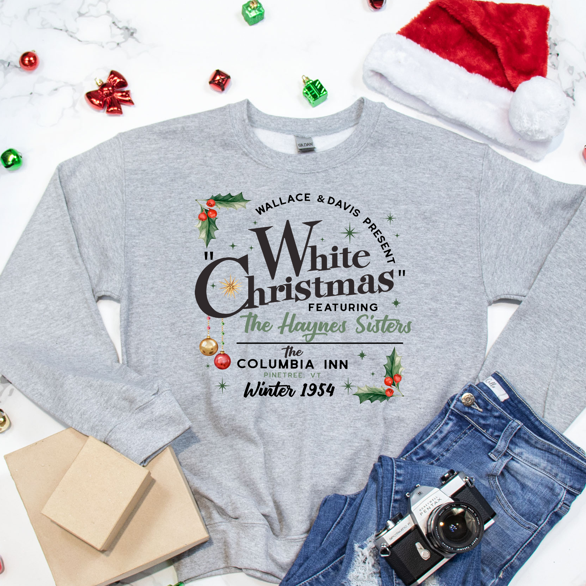 Gray sweatshirt with Christmas-themed text, surrounded by festive items like a Santa hat, camera, and presents.