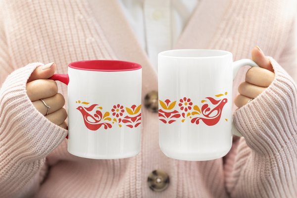 Two mugs with decorative designs held by a person wearing a light pink sweater.