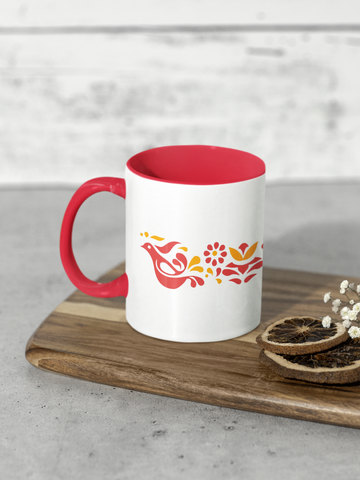 White mug with red interior and handle on a wooden board with dried leaves and flowers.