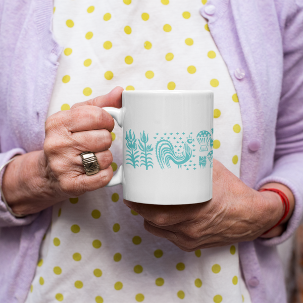 Person holding a mug with a design, wearing a polka dot apron and light purple cardigan.