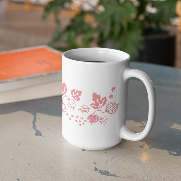 White mug with pink floral design on a glass table with a book and plant in the background