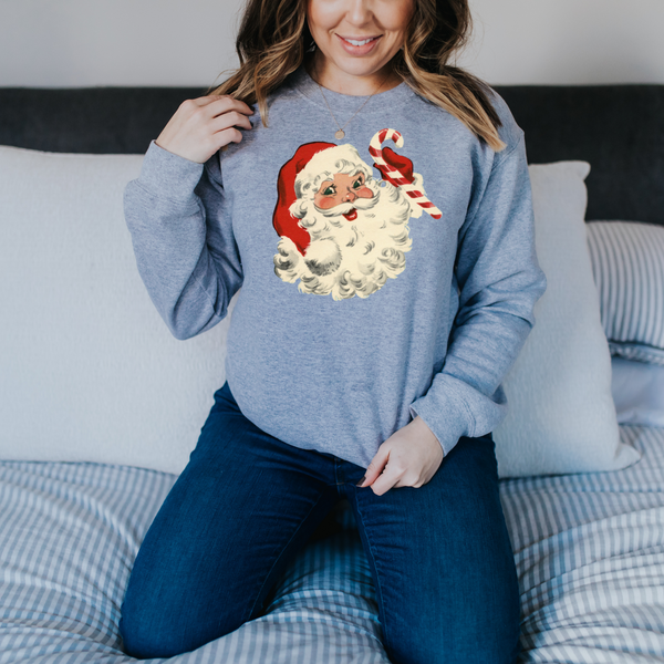 Woman wearing a blue sweatshirt with a Santa Claus graphic sitting on a bed.