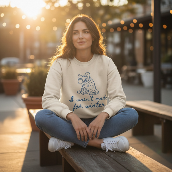 Woman sitting on a bench wearing a light-colored sweatshirt with a graphic design and text.